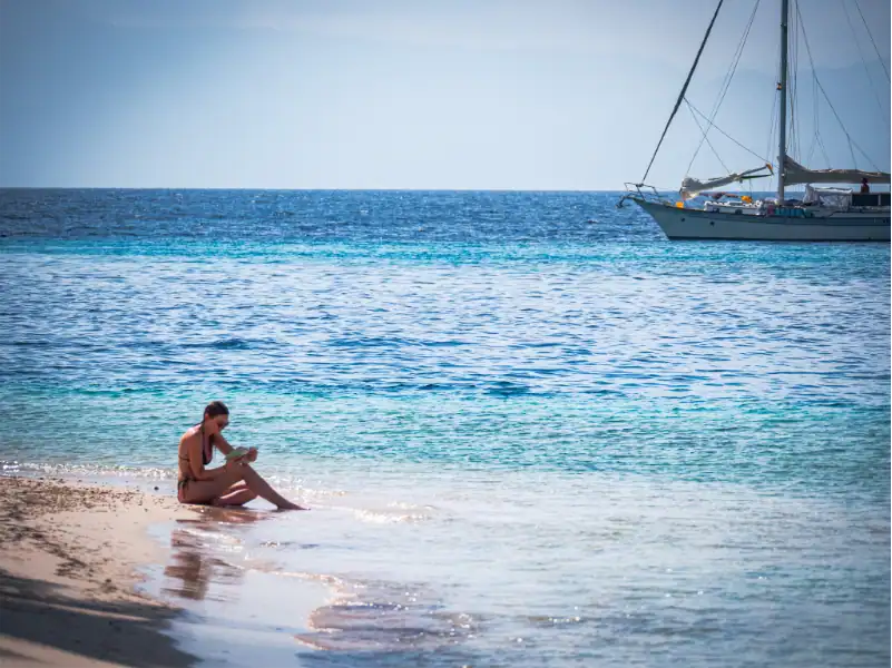 Entspannter Mensch liest am Strand vor einer Yacht in den San Blas Inseln.