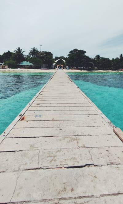 Holzsteg auf den San Blas Inseln, Panama, mit türkisfarbenem Wasser und Palmen im Hintergrund.