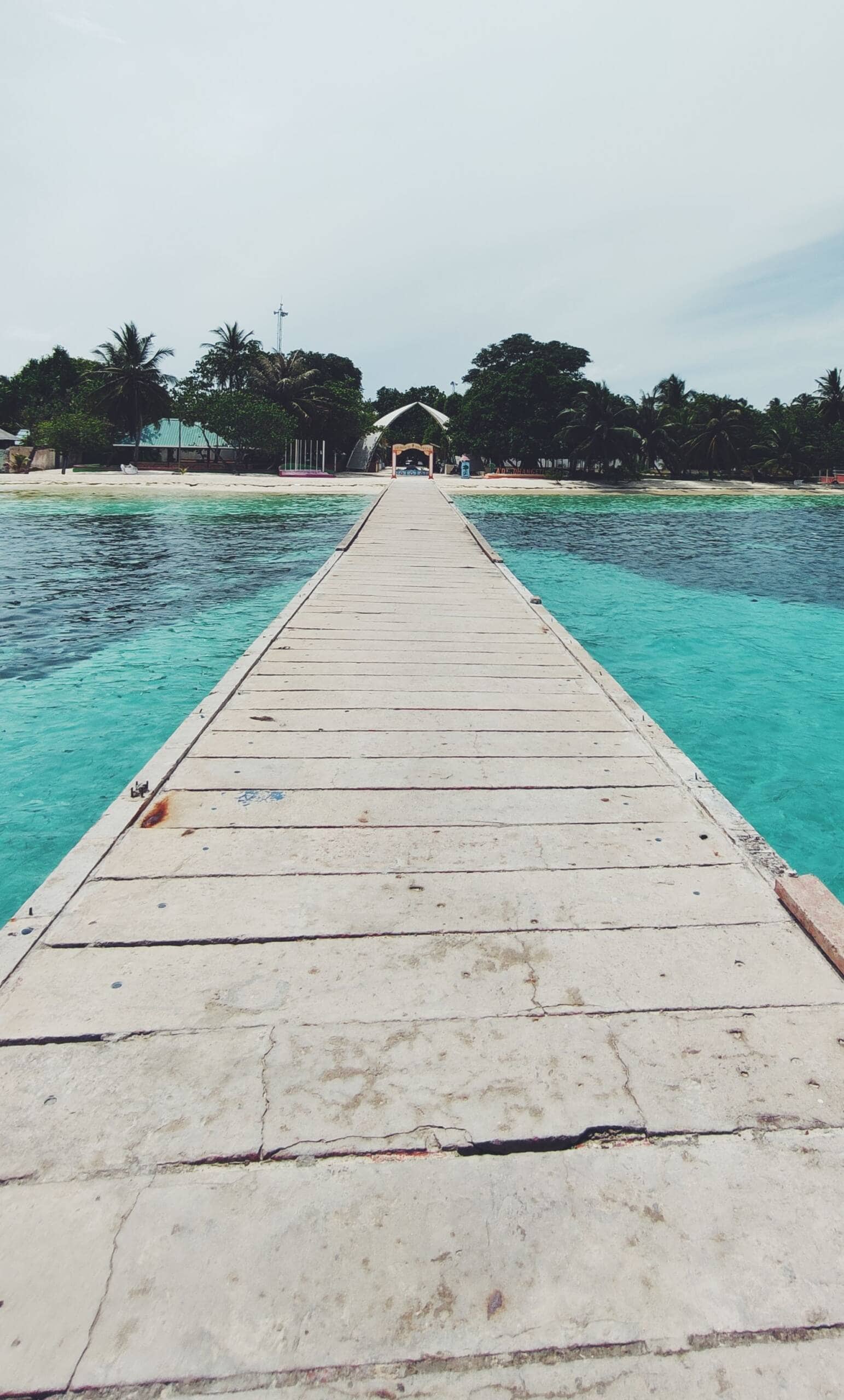 Holzsteg auf den San Blas Inseln, Panama, mit türkisfarbenem Wasser und Palmen im Hintergrund.
