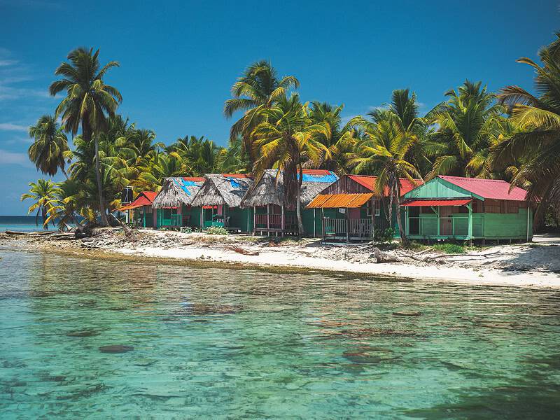 Bunte Hütten an der Küste der San Blas Inseln, Panama, mit Palmen und klarem Wasser.